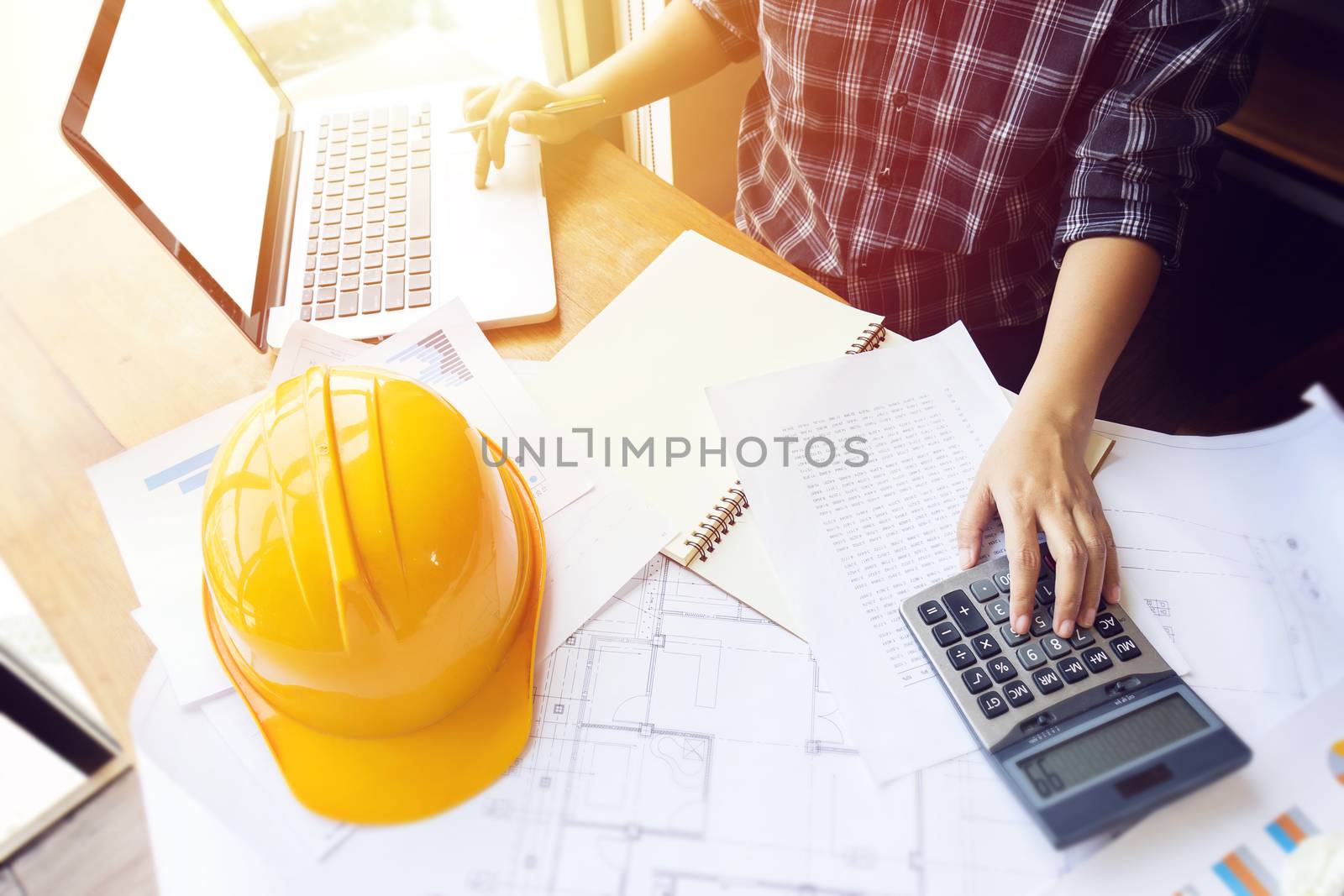 Asian engineer , architect woman using calculator for accounting and analyzing building structure from blueprint and paper chart in front of computer laptop at office work space. by asiandelight