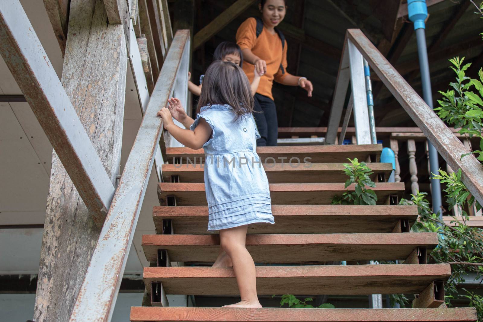 Asian little child girl walking up on wooden stair in restaurant. Dangerous in children. by TEERASAK