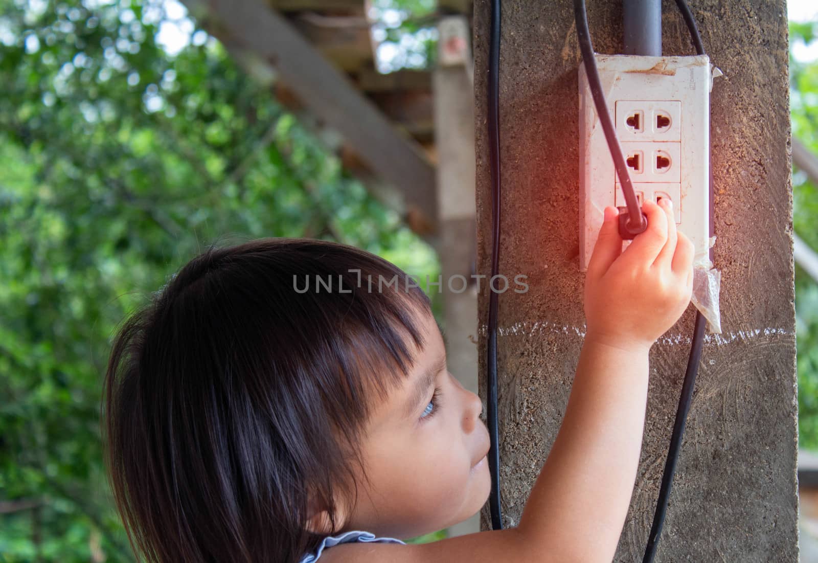 Asian little child girl is plugging in the socket . Dangerous situation in children. by TEERASAK