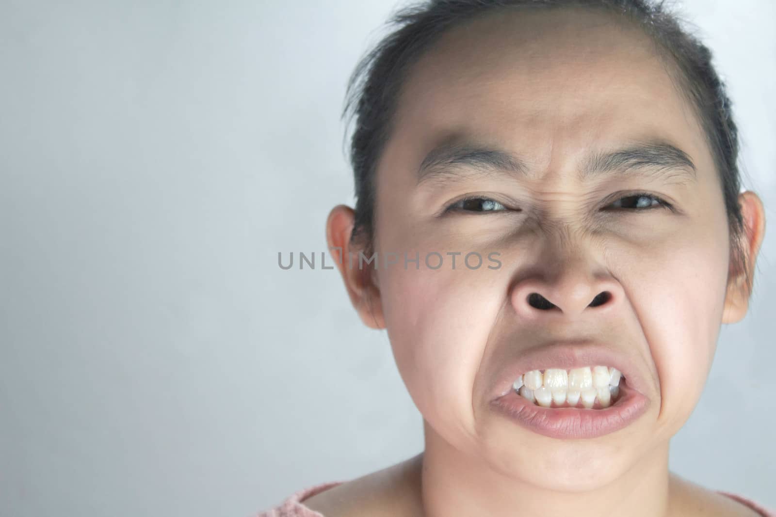 Portrait of Asian woman with hate and disgusting face in pink shirt on grey background.
