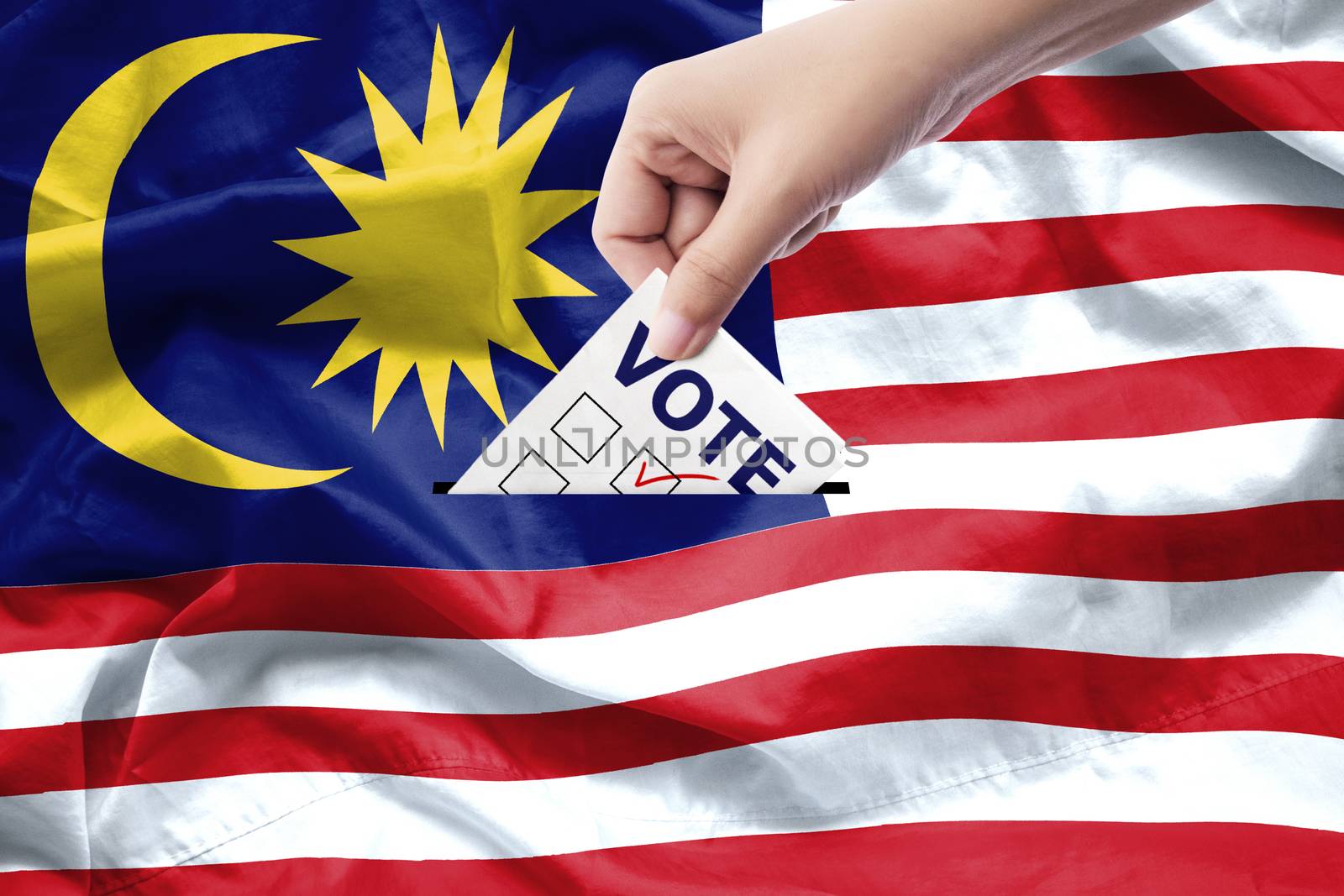 Malaysia general election concept. close up hand of a person casting a ballot at elections during voting on canvas Malaysia flag background. by asiandelight