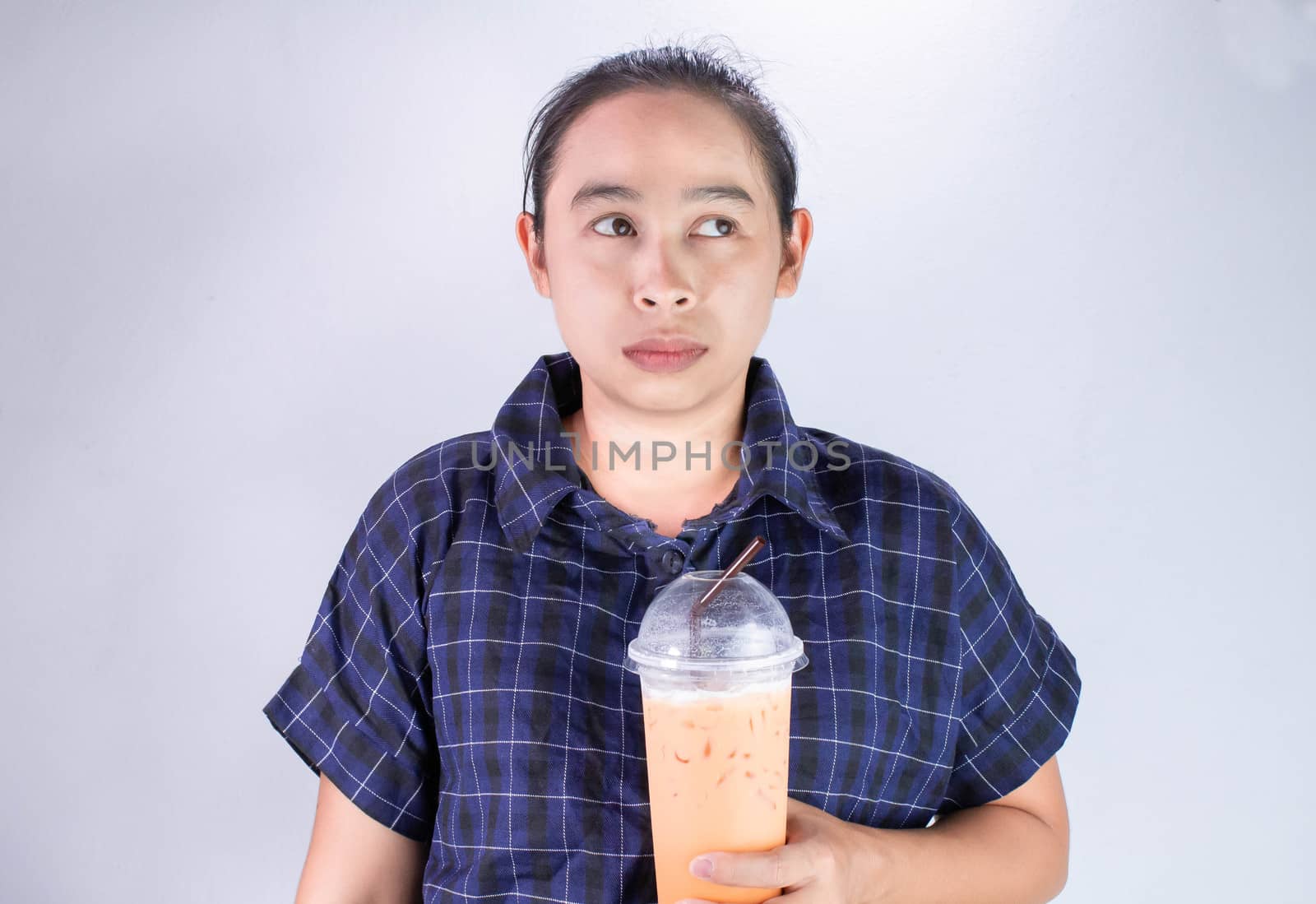 Serious Asian young woman holding Thai tea with milk in plastic glass and look at empty space beside.