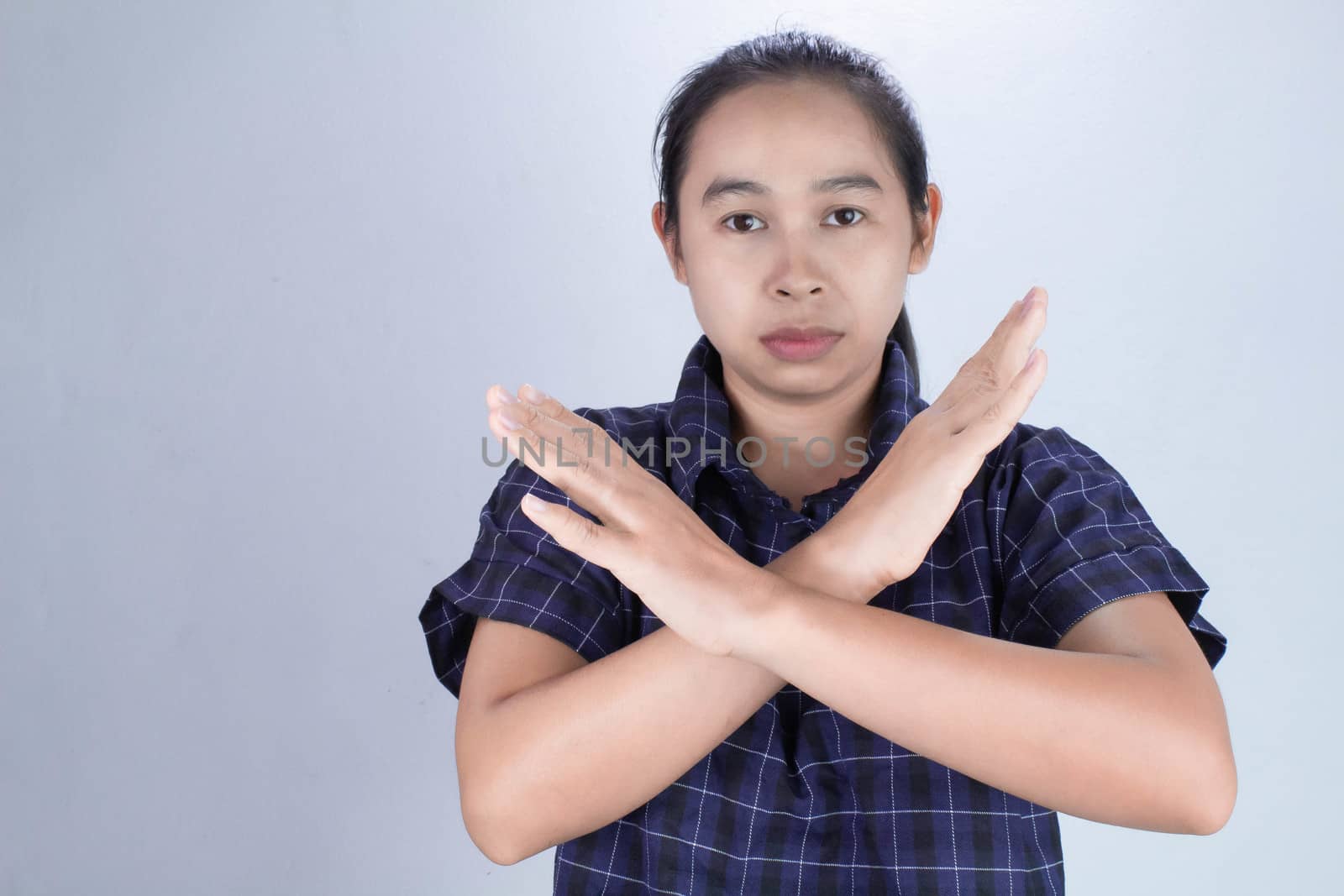 Portrait of Asian young woman in blue shirt, show X sign on hands with Serious face isolated on grey background. Concept of rejection. by TEERASAK