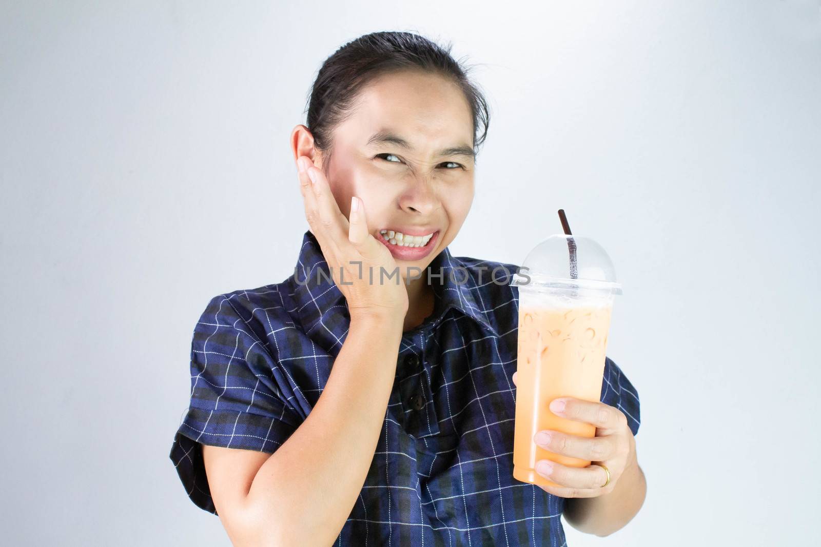 Asian young woman touching cheek with hand because she tooth sensitivity and toothache from drinking cold water. Dental care and health concept. by TEERASAK