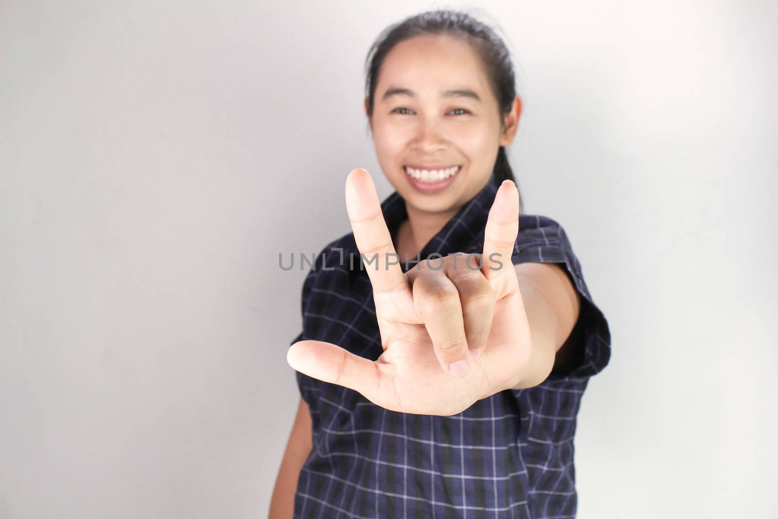 Portrait of Asian young woman in blue shirt, Showing I LOVE YOU with body language and smiley face isolated on grey background. Concept of love and concern.