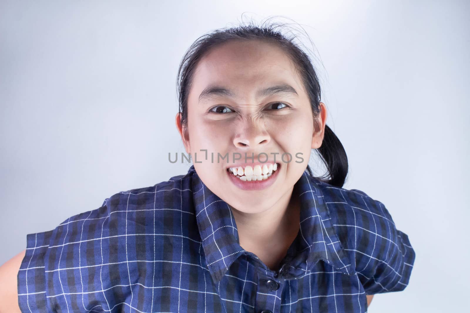 Close-up Angry face of Asian young woman in blue shirt with look to the camera. by TEERASAK