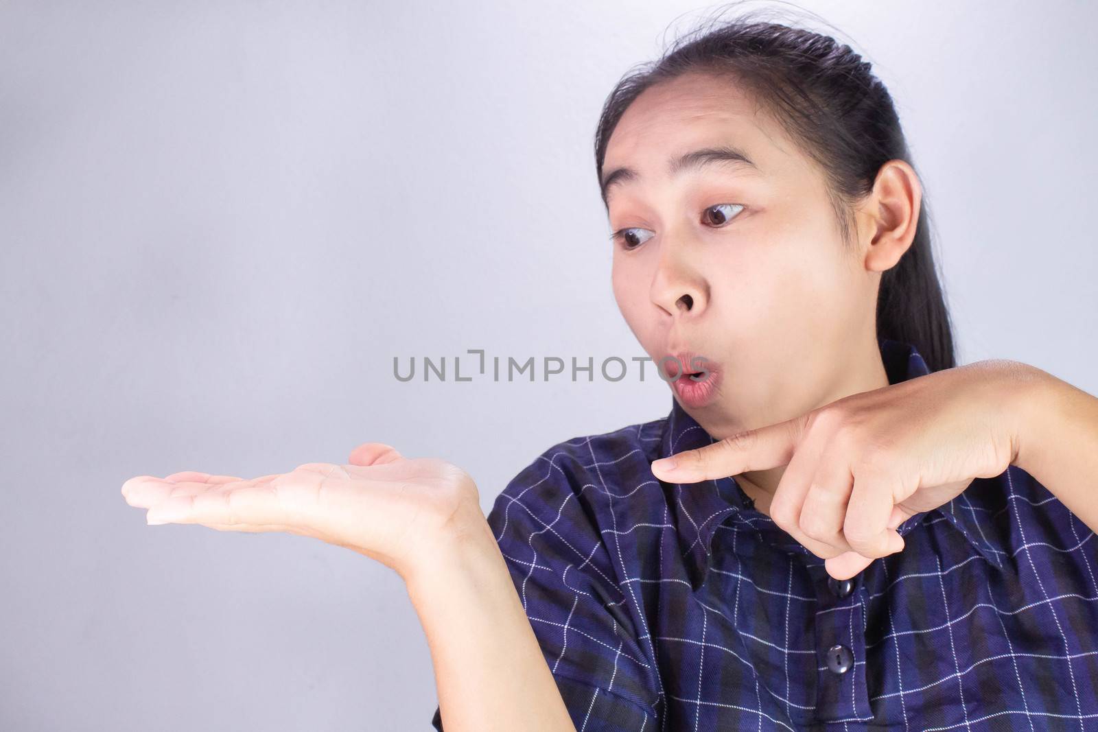 Close-up wow and surprised face of Asian young woman wearing blue shirt with hand point on empty space.
