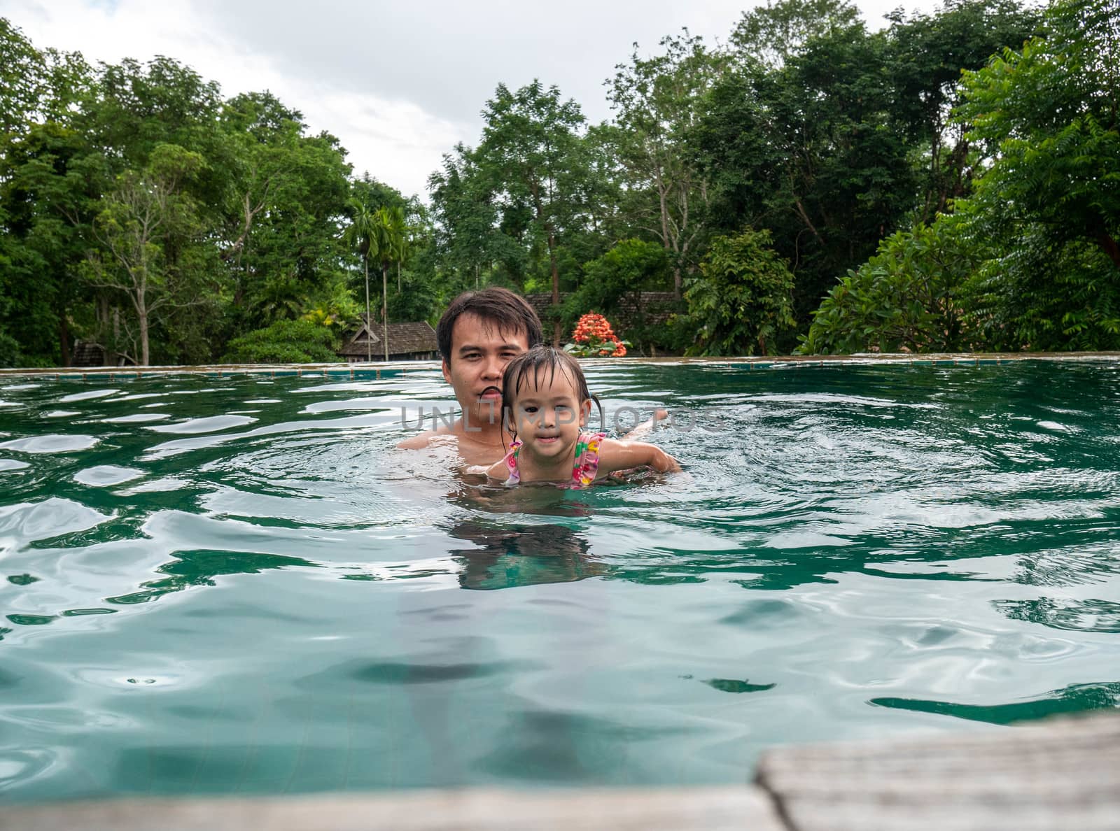 Portrait of Father and daughter enjoying a summer holiday in swimming pool at Northern resort of Thailand.