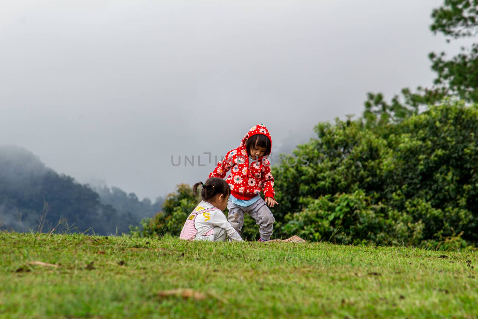 Asian little child girl helped to put shoes on the sister on the grass at Ang Khang mountain, Fang Chiang Mai. Tourist attraction in northern of Thailand.