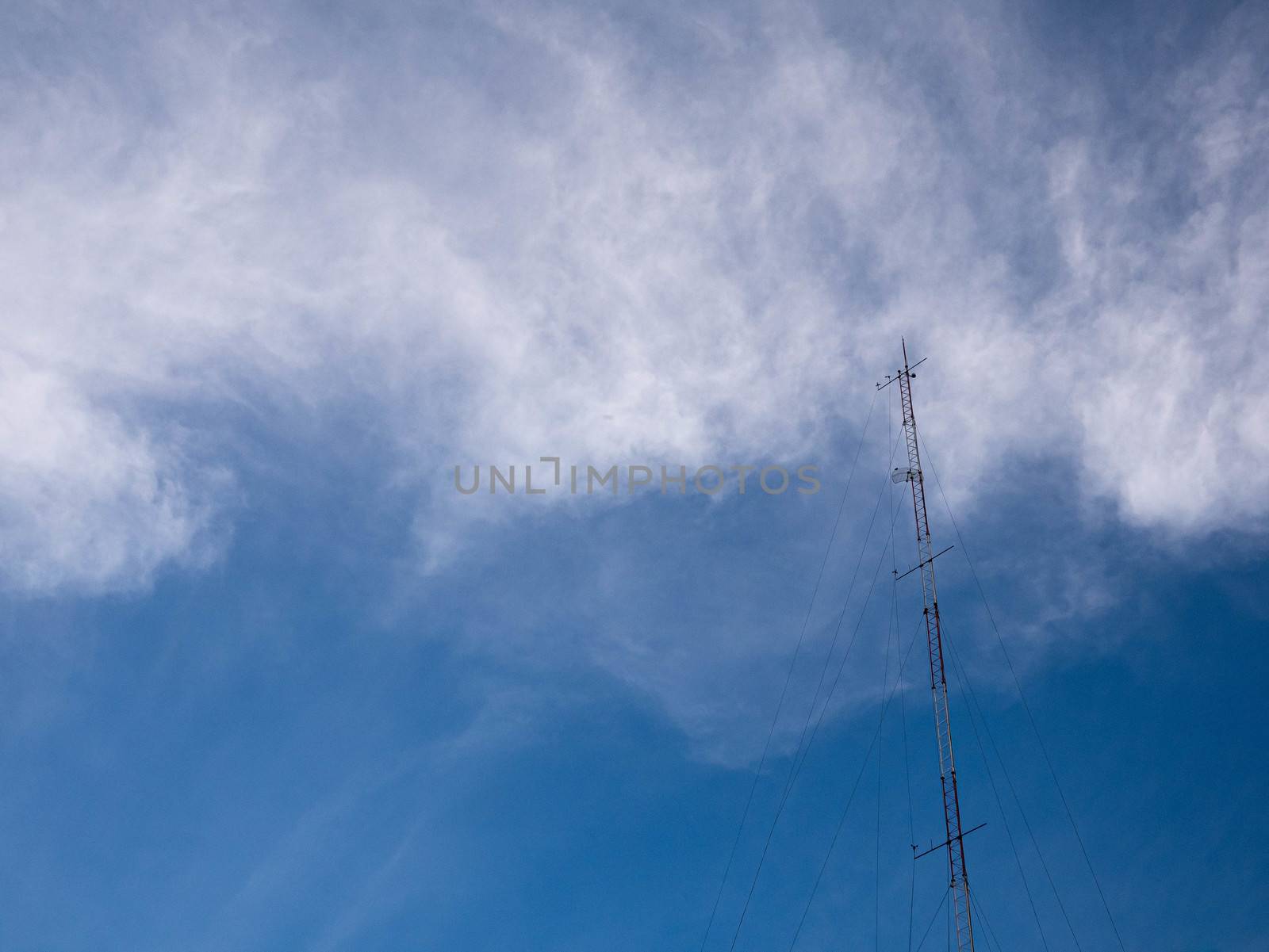 TV and radio pole telecommunication antenna on clouds and blue sky background.