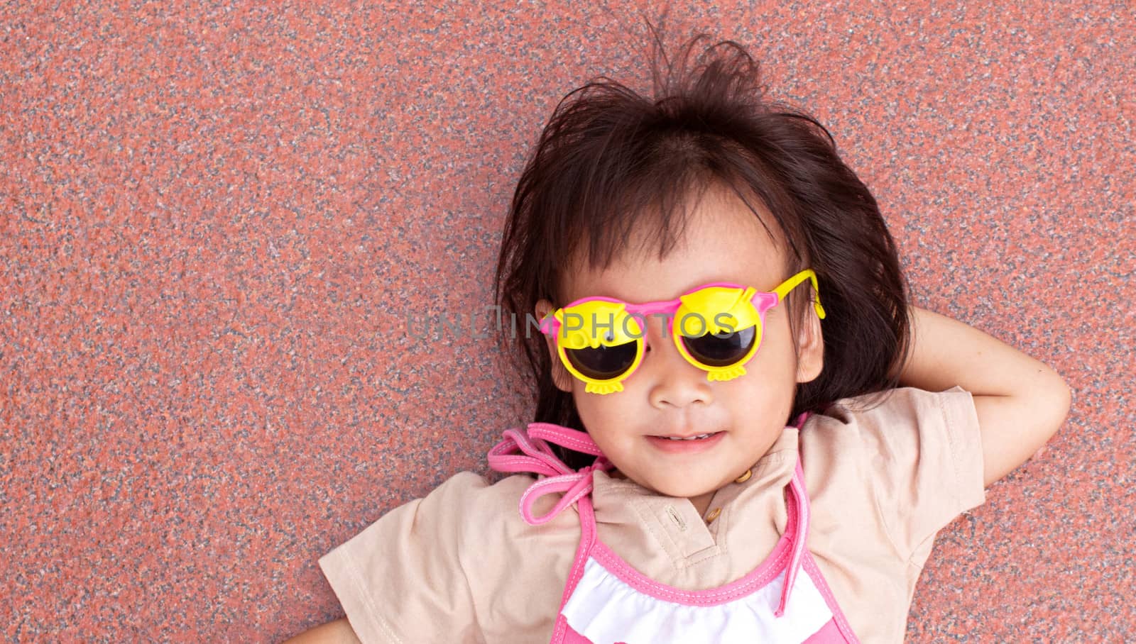 Asian little child girl wearing yellow glasses with smile face and lying on the floor happiness. by TEERASAK