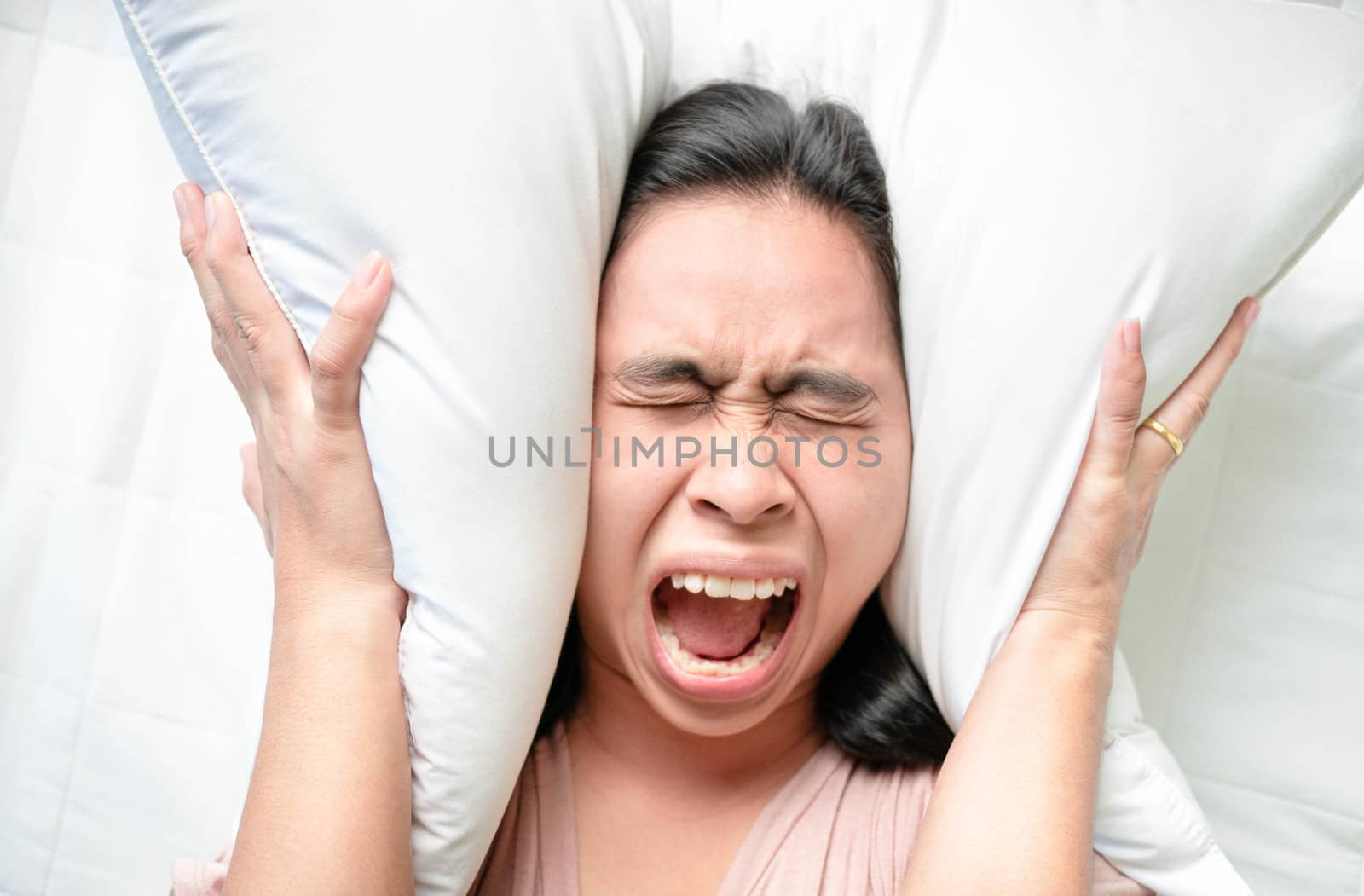 Asian young woman used pillow over her ears while alarm clock on bed in the morning.