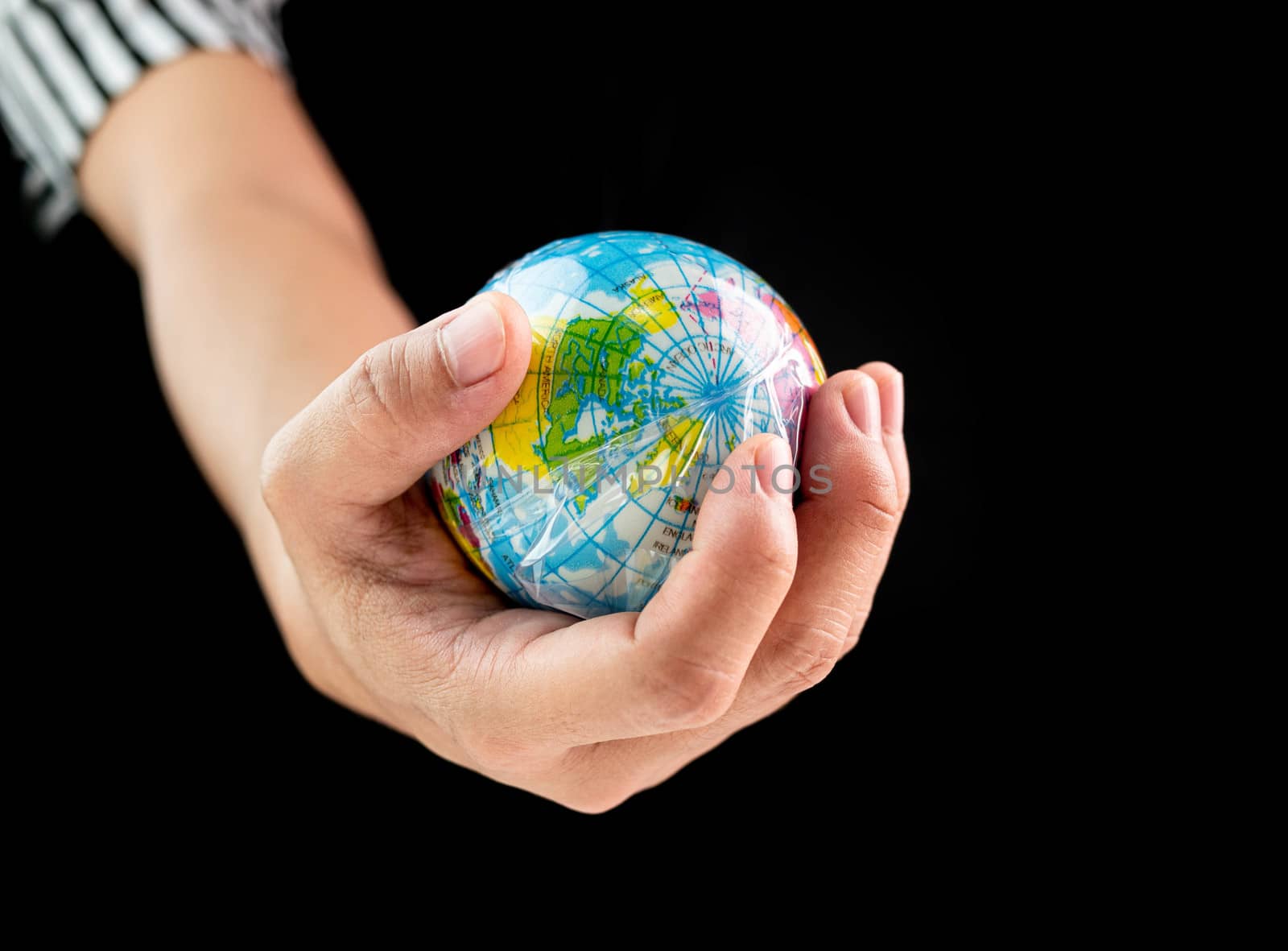 Woman hand holds the earth in plastic bag on black background. Global warming due to pollution by plastic debris. The concept of Earth Day.