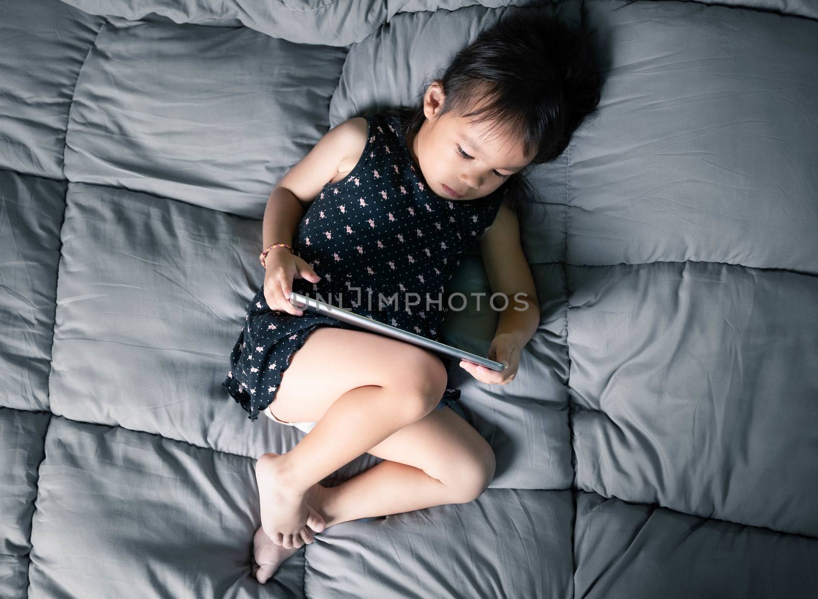 Asian little girl watching laptop on their bed. Kid addicted to mobile phones.