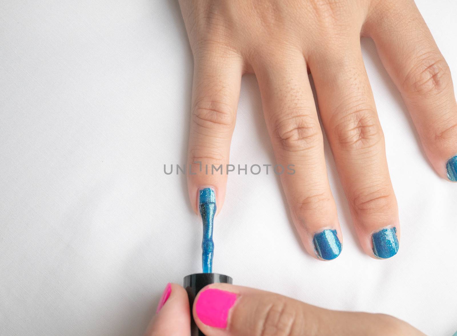Close-up of female hands painting blue nail varnish, self made manicure at home. by TEERASAK