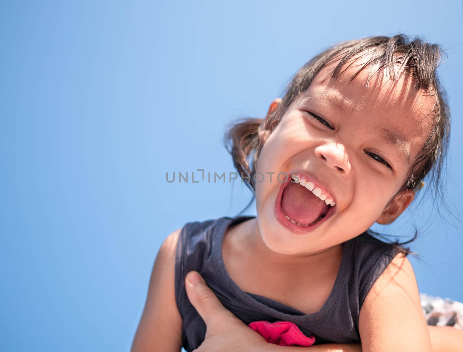 Adorable Asian child girl having fun in spring, smiling and looking at camera of bright sky background.