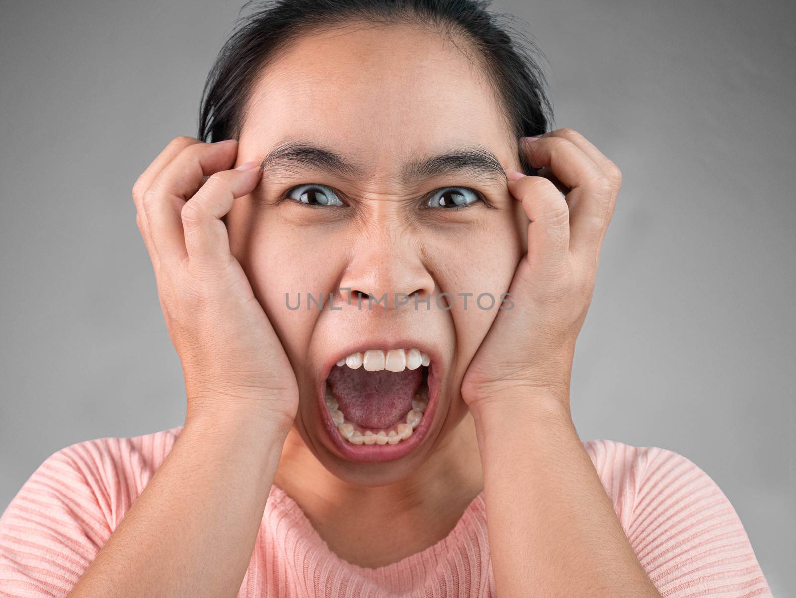 Furious and frustrated woman yelling with hand on face, Isolated on grey background. Emotional and expression concept. by TEERASAK