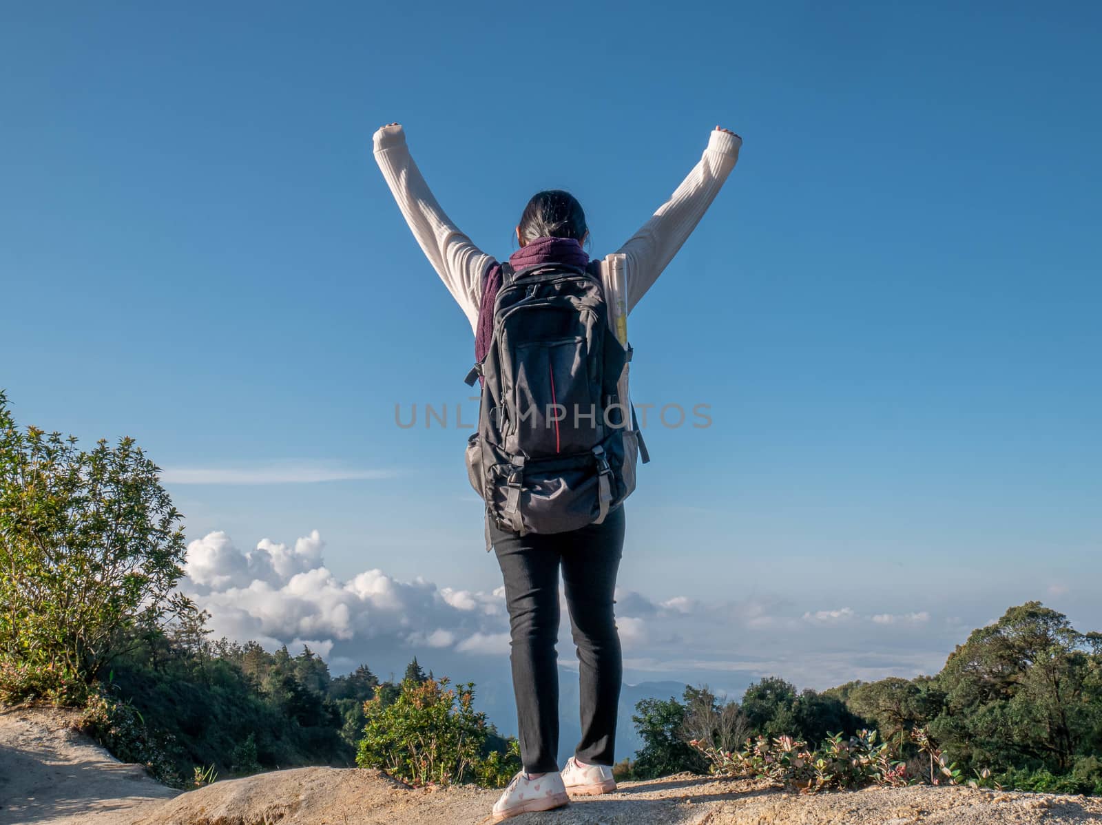 Young woman traveler raise arms to show success at peak of mountains on summer vacations day. Lifestyle hiking concept.