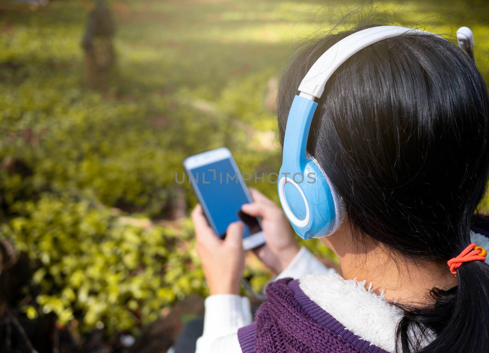 Asian young girl listening to music by headphone in the garden. Technology and relaxation concept.