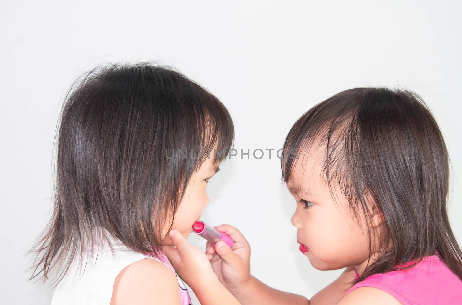 Asian child girl apply red lipstick on lips for sister on white background. by TEERASAK