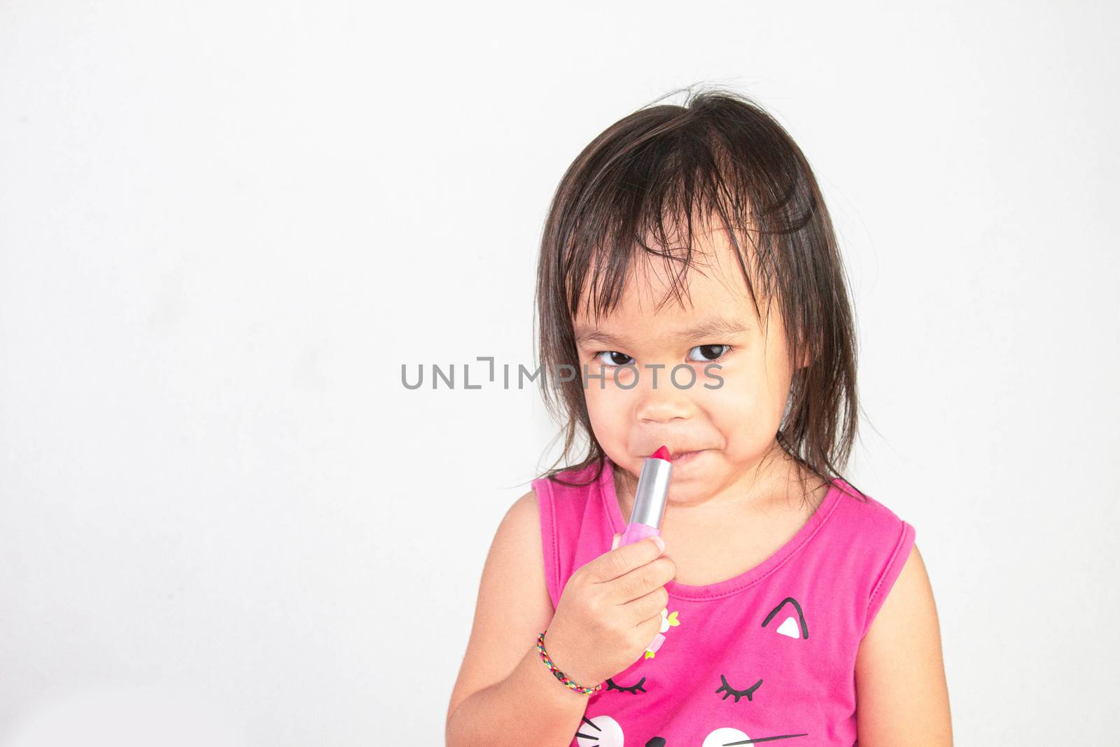 Happy Asian child girl with apply red lipstick wearing pink dress isolated on white background.