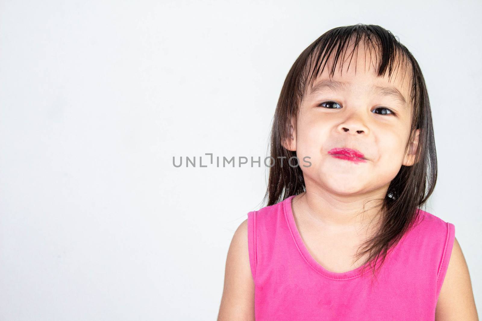 Happy Asian child girl with apply red lipstick wearing pink dress isolated on white background. by TEERASAK