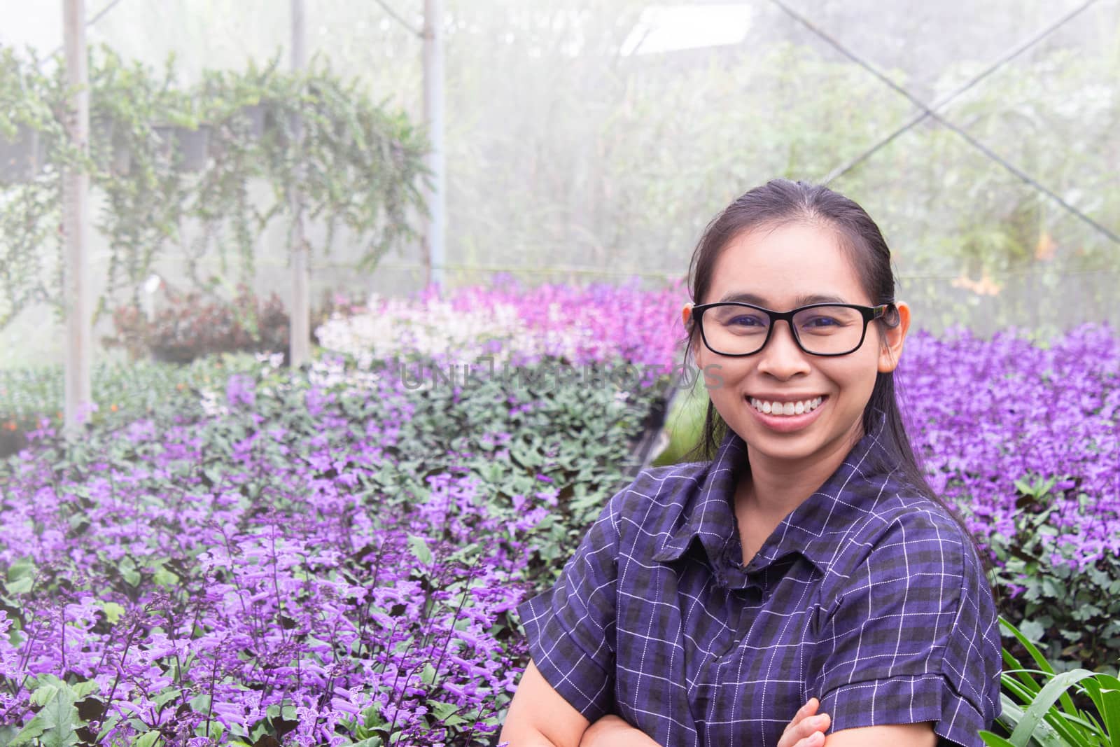 Gardener Asian woman standing and cross one's arm proud in the growing flowers in greenhouse. by TEERASAK
