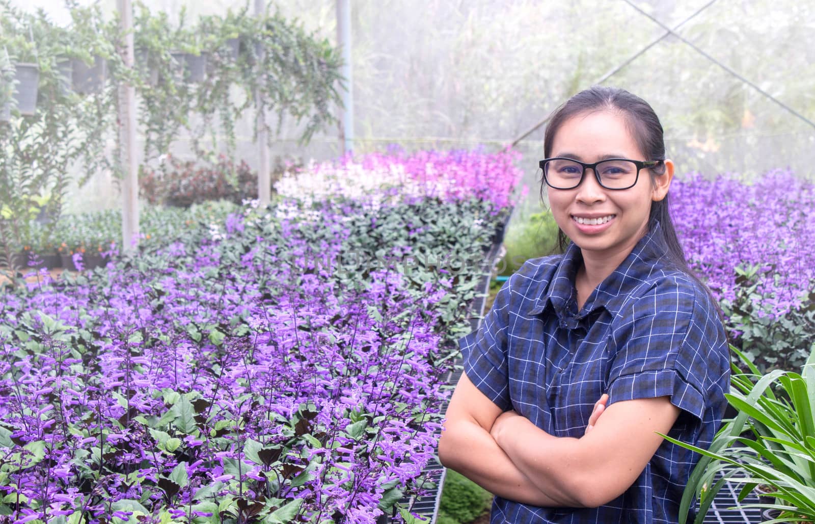 Gardener Asian woman standing and cross one's arm proud in the growing flowers in greenhouse. by TEERASAK