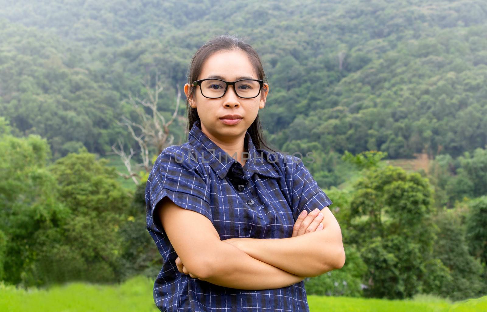 Asian farmer woman smile and cross one's arms with a look of proud on rice field background. by TEERASAK