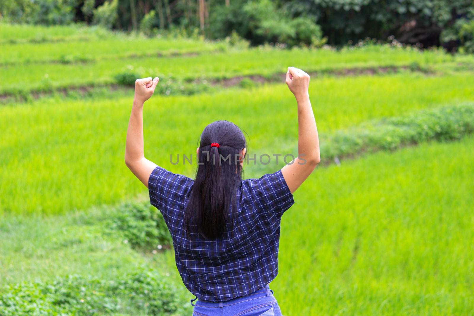 Rear of Asian young woman stand and raising her arms with a look of success on nature background.