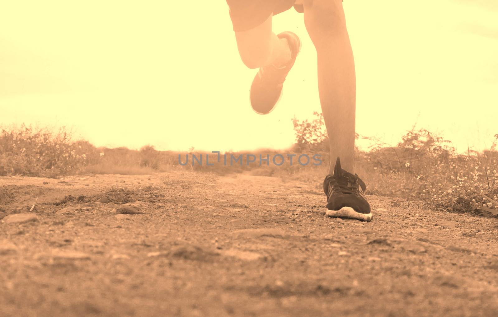 Close-up Legs of Asian young man is jogging on dirt road in the park. Healthy lifestyle. by TEERASAK