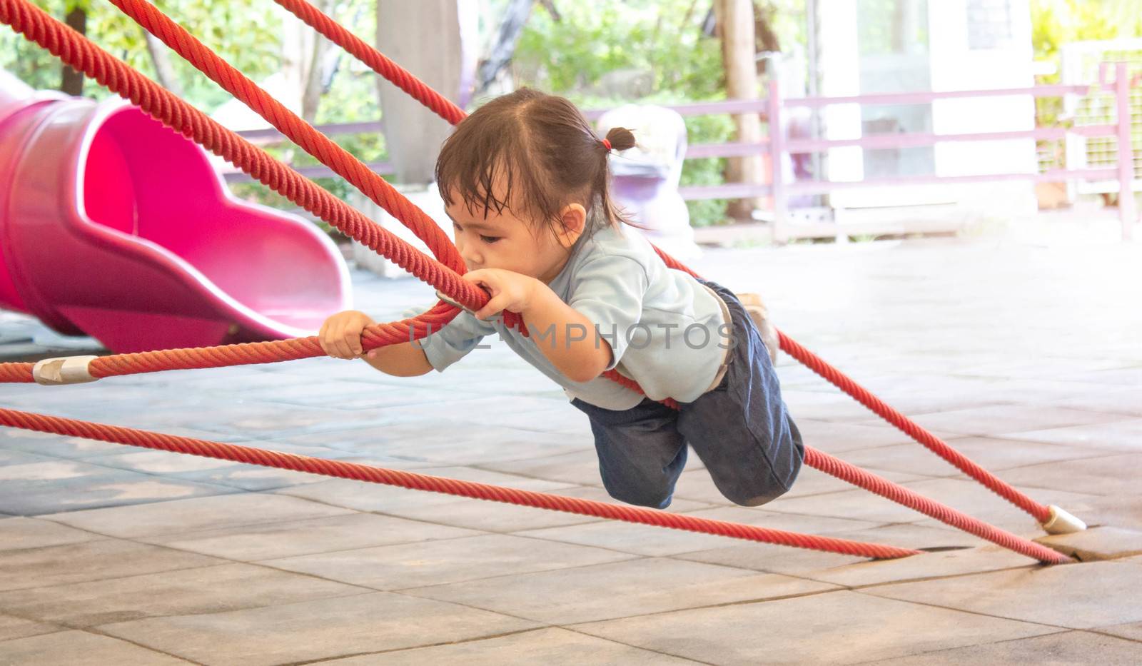 Asian little child girl having fun to climbing rope at playground in summer time. by TEERASAK