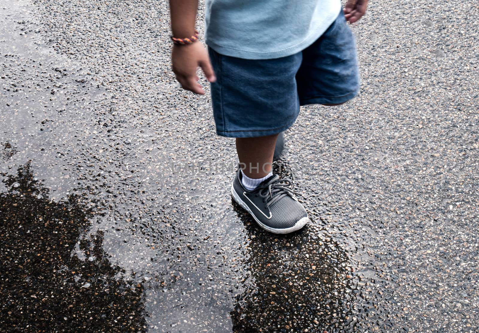 Legs of Asian little child walking through in puddle on the street.