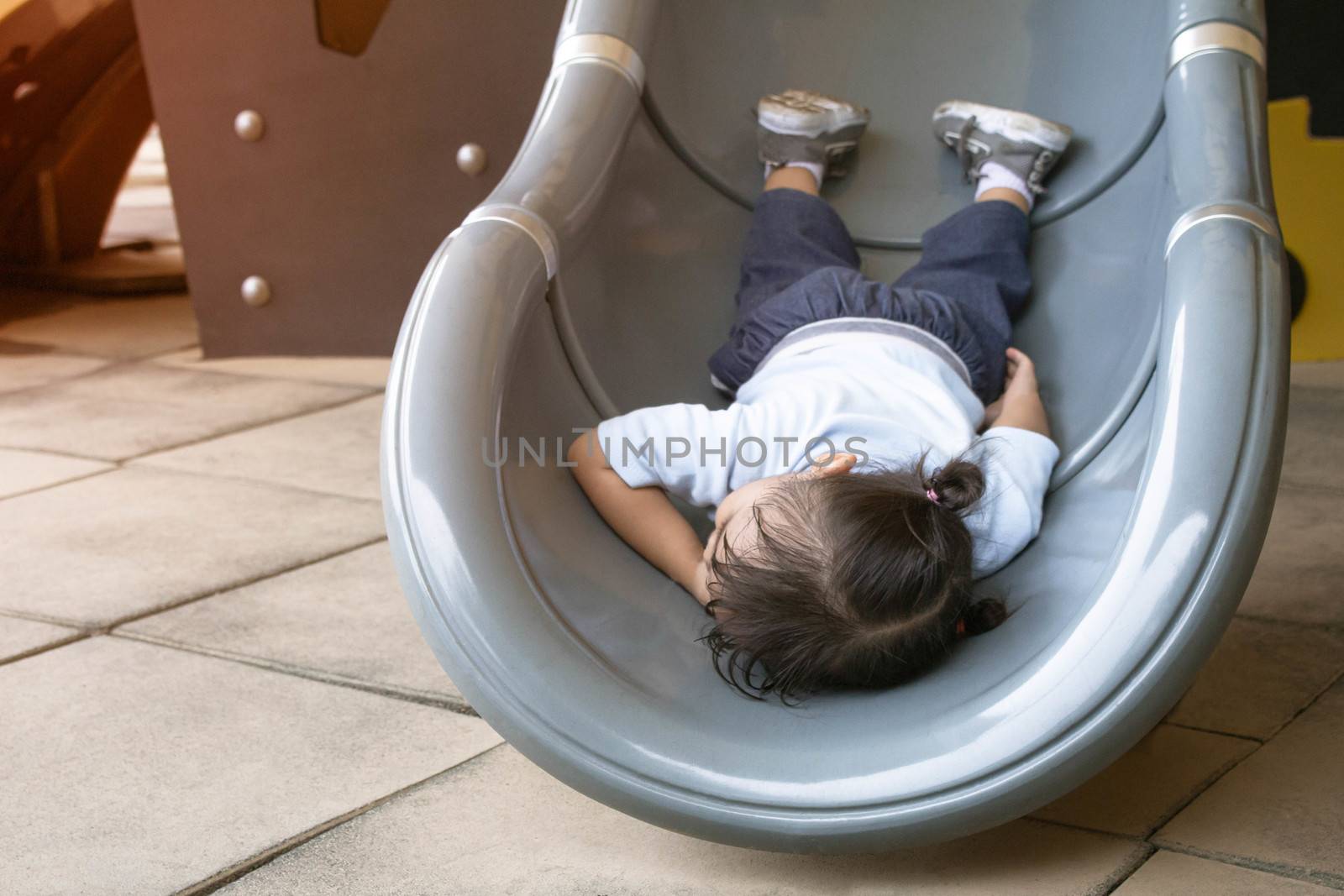 Asian little child girl is tired and lying on slide at playground.
