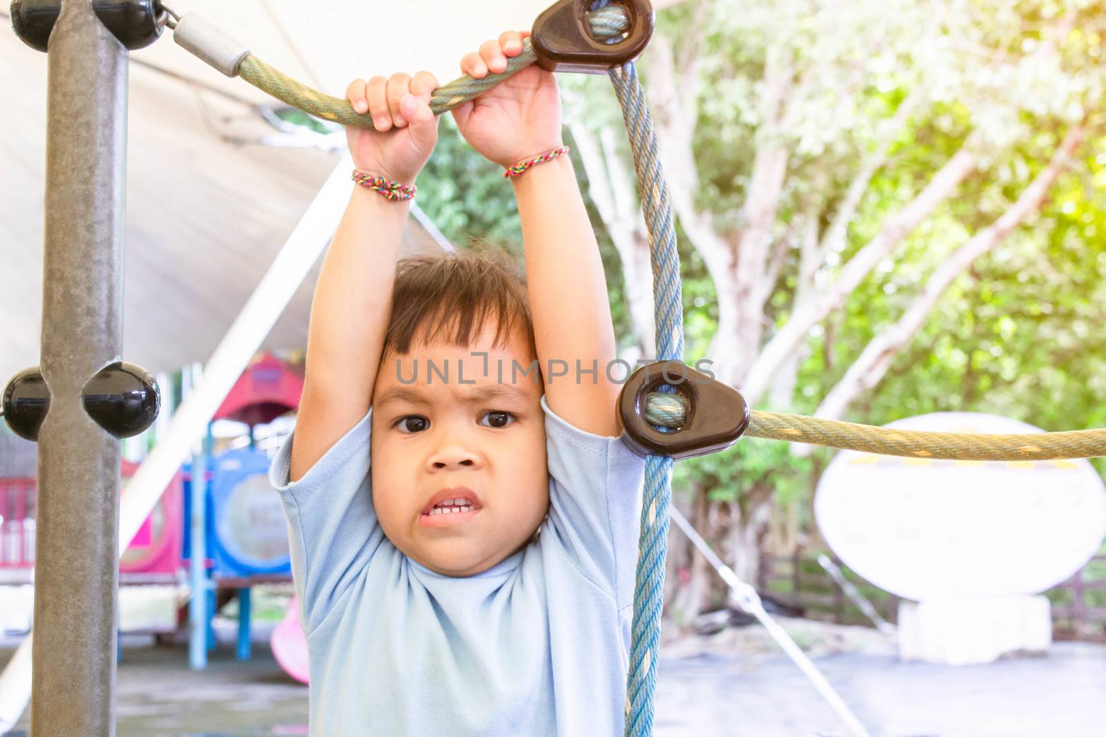 Asian little child girl afraid of falling while climbing rope at playground in summer time.