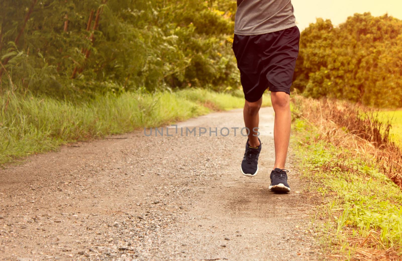 Close-up Legs of Asian young man is jogging on dirt road in the  by TEERASAK