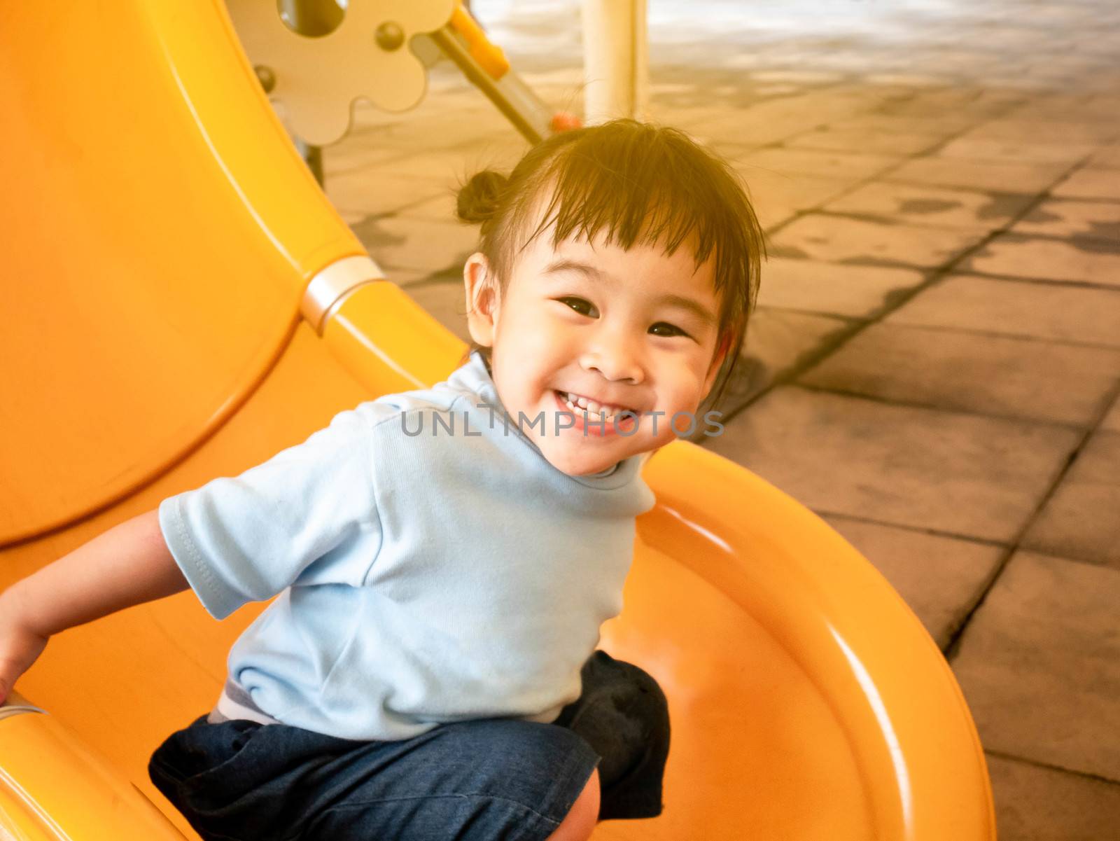 Happy Asian little child girl having fun on slide at playground.