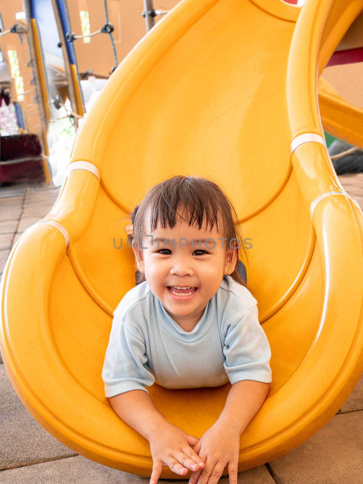 Happy Asian little child girl having fun on slide at playground.