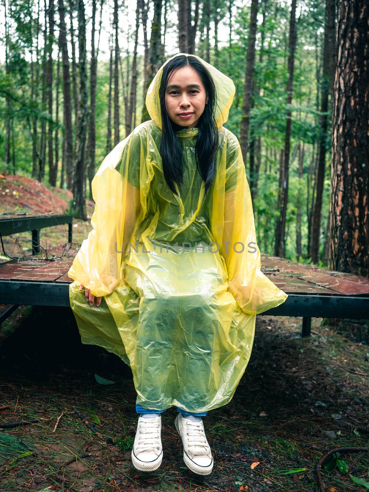 Happy Asian woman wearing yellow raincoat sitting on wooden stag by TEERASAK