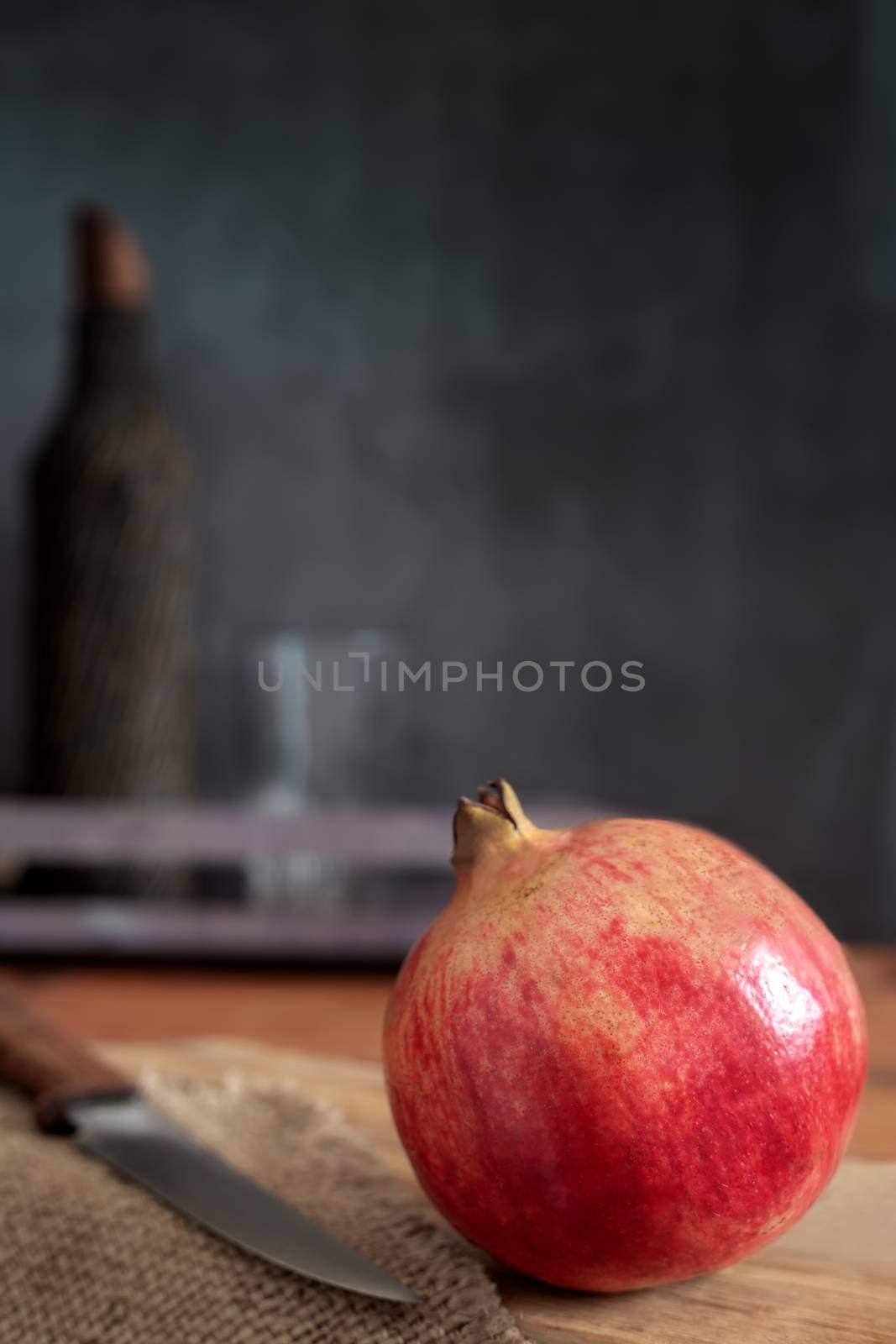 On the kitchen table on the cutting Board is a large ripe pomegranate fruit. Next to it is a kitchen knife. A dark background and copy space.