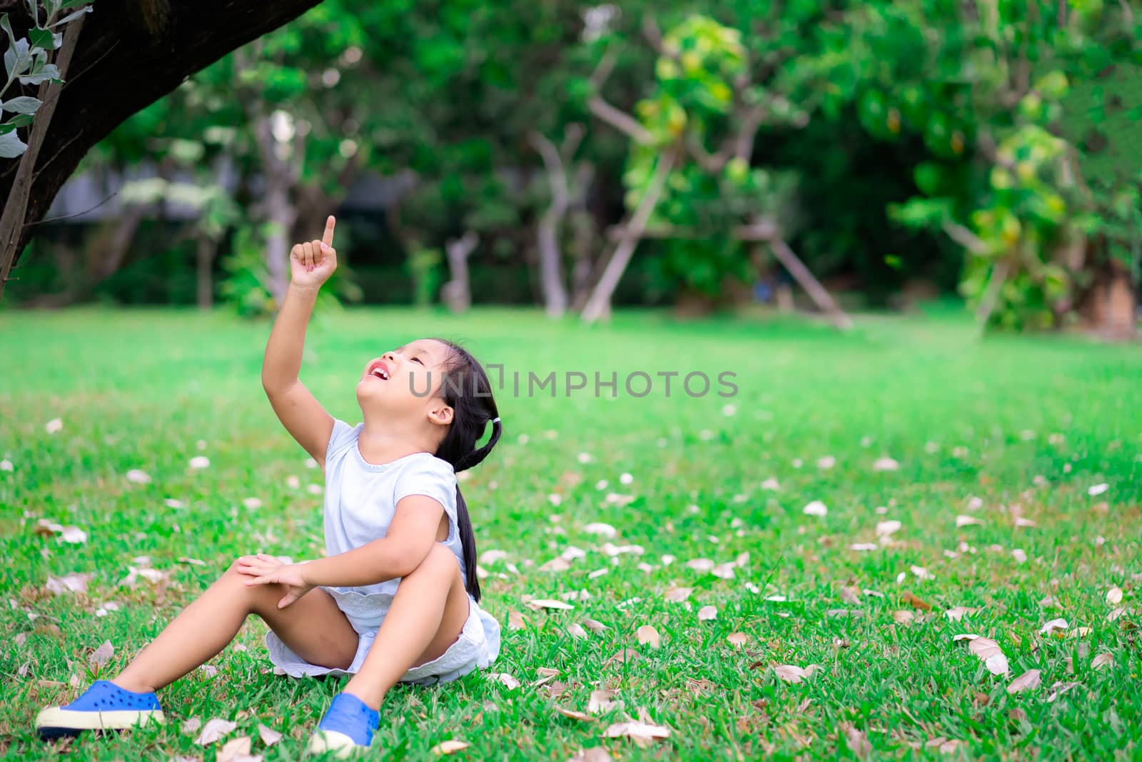 Cute little asian girl sitting on grass pointing to the sky