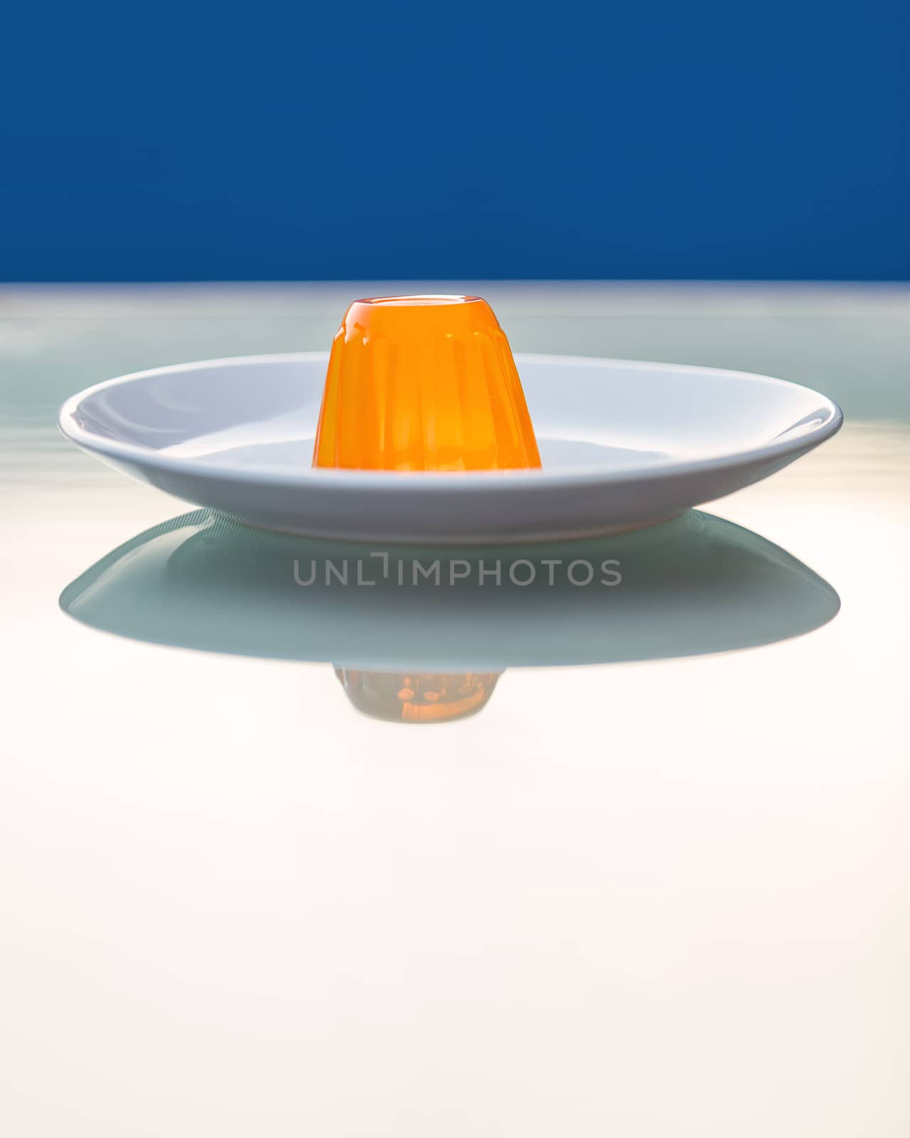 Close-up of an orange gelatin on a white plate reflected on a glass table