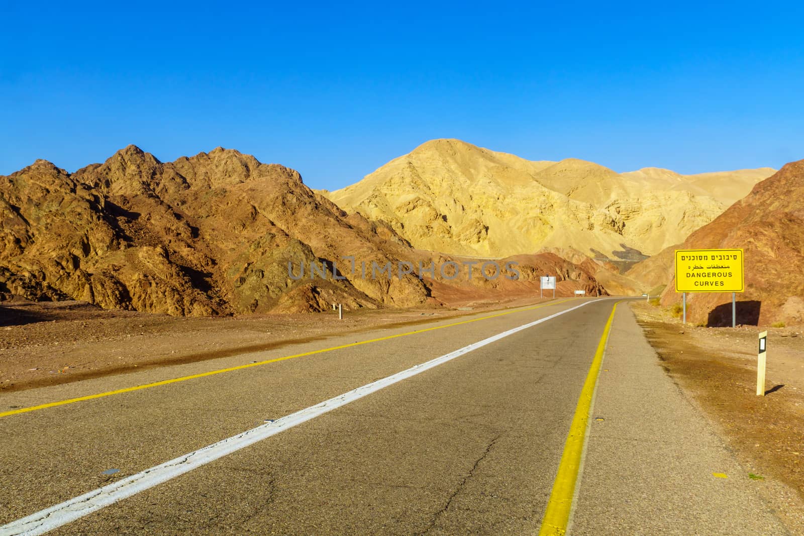 View of desert road 12, with a trilingual warning sign (dangerous curves) and landscape. Eilat mountains, southern Israel