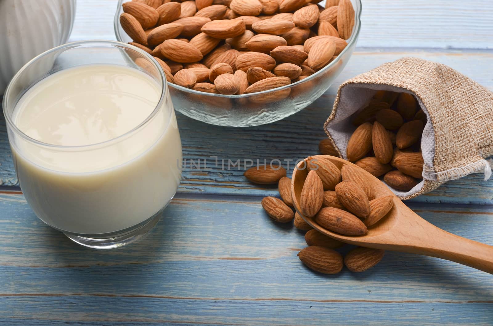 Close up view of healthy almond milk in drinking glass with seed in bowl on wooden background. Selective focus.