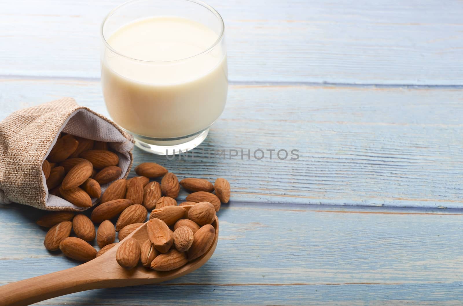 Close up view of healthy almond milk in drinking glass with seed in bowl on wooden background. Selective focus.