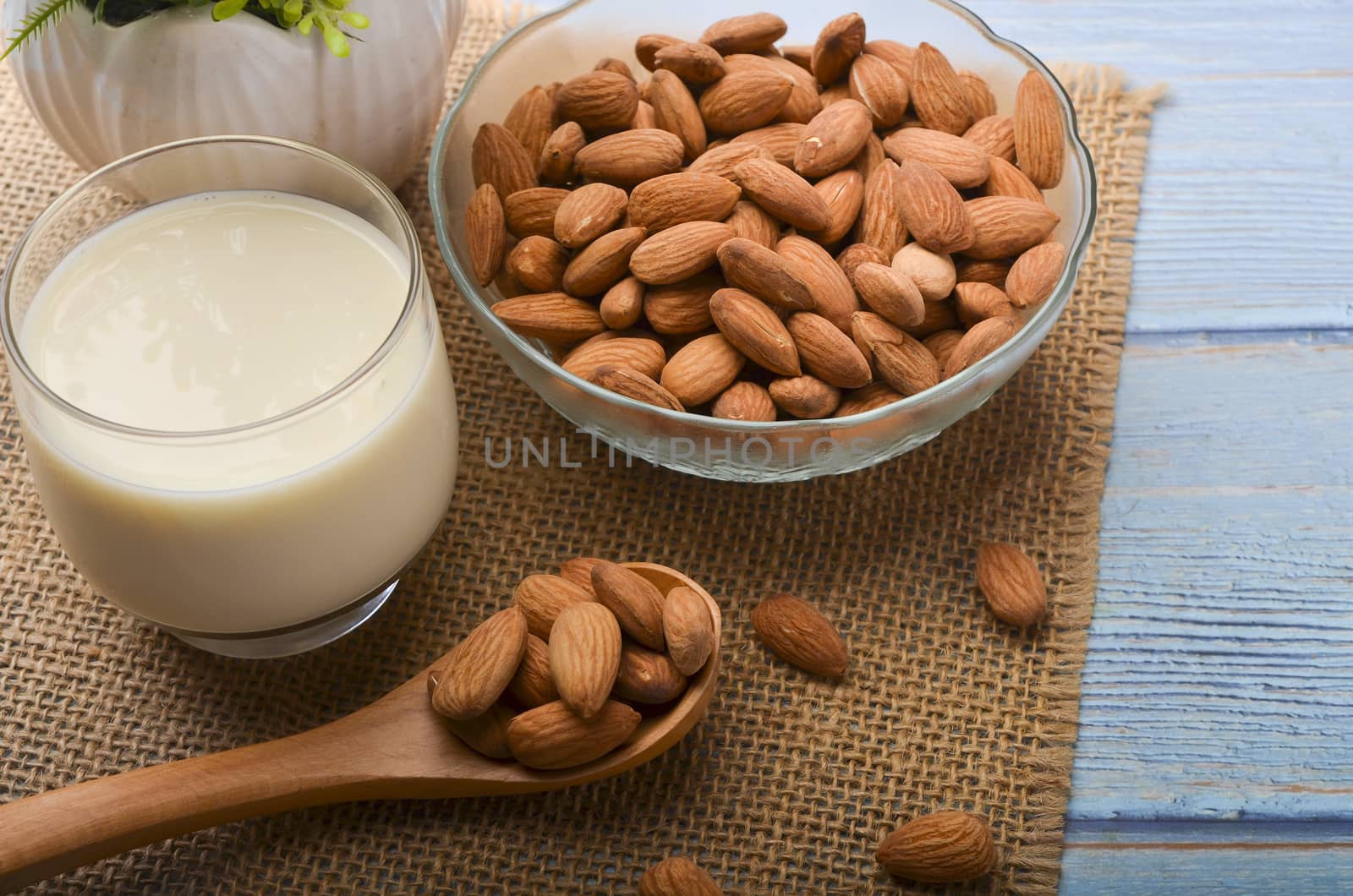 Close up view of healthy almond milk in drinking glass with seed in bowl on wooden background. Selective focus.