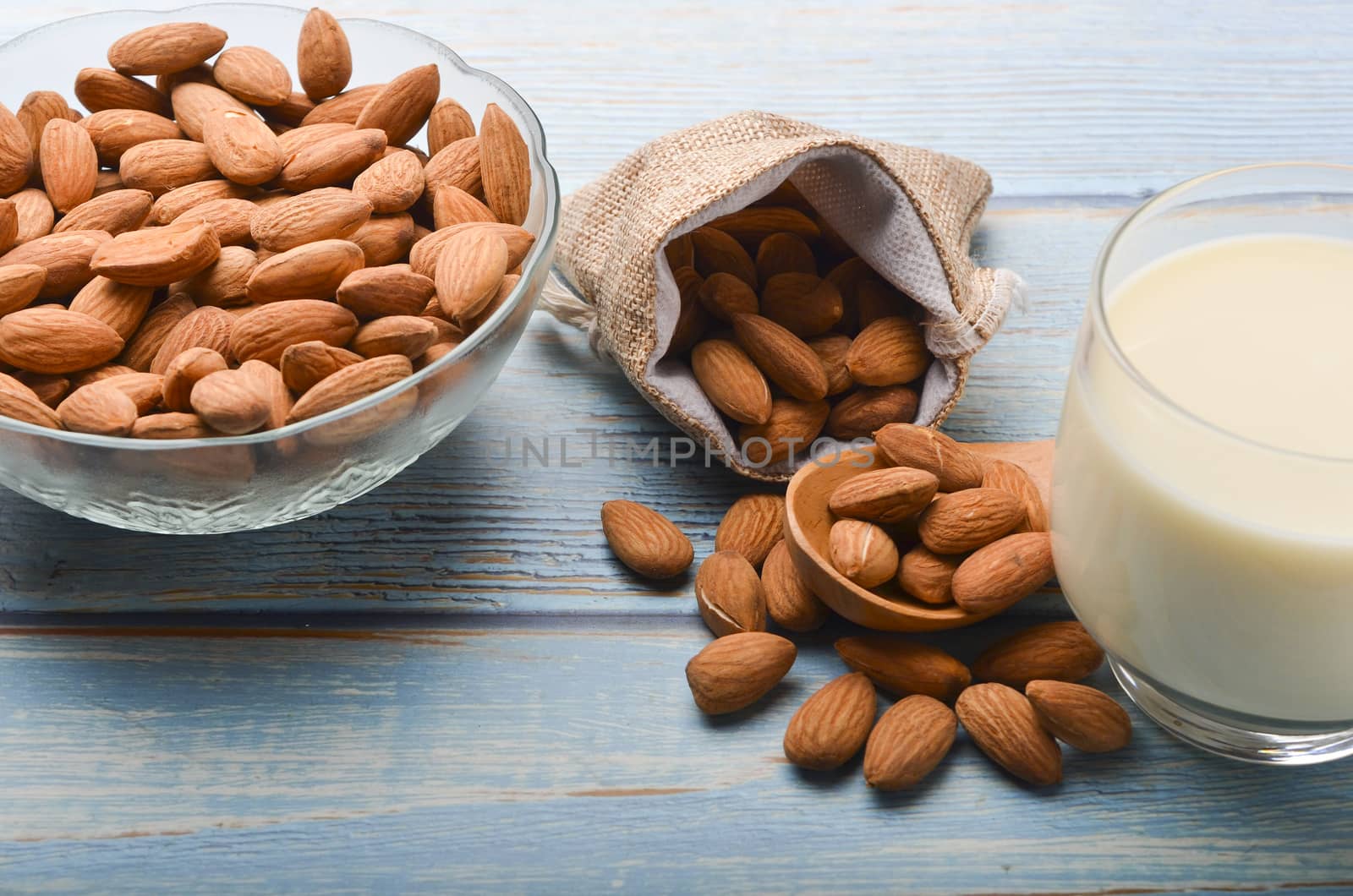 Close up view of healthy almond milk in drinking glass with seed in bowl on wooden background. Selective focus.