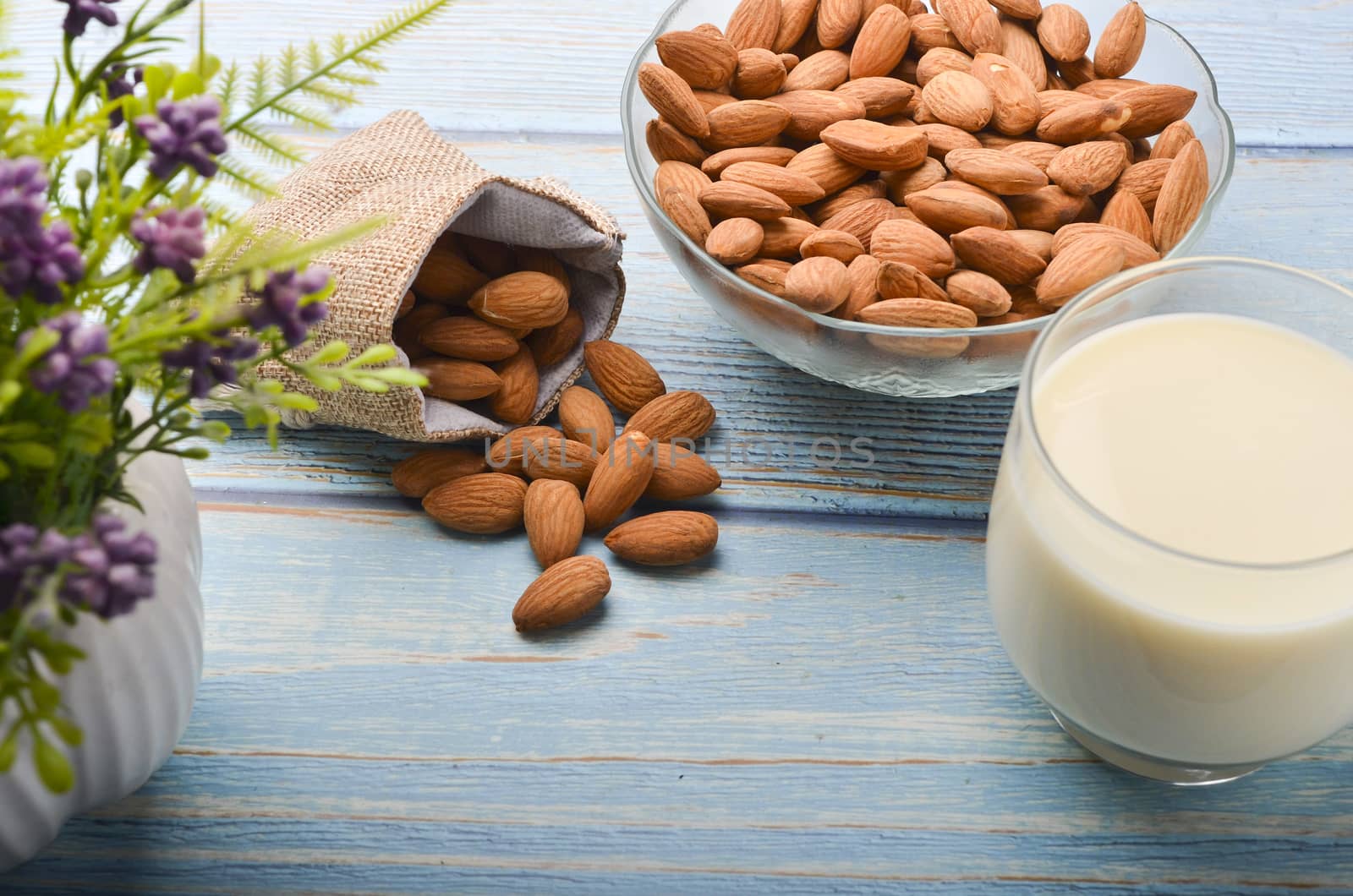 Close up view of healthy almond milk in drinking glass with seed in bowl on wooden background. Selective focus.