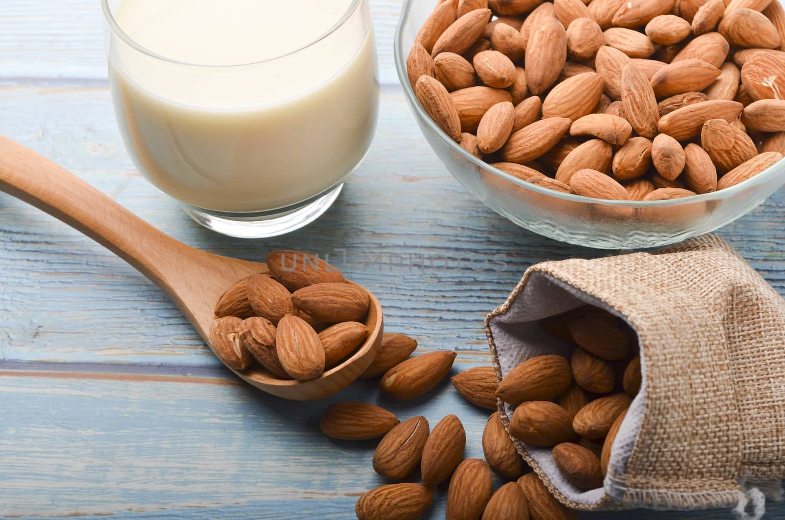 Close up view of healthy almond milk in drinking glass with seed in bowl on wooden background. Selective focus.