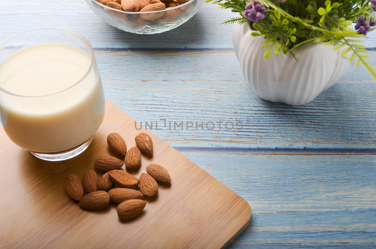 Close up view of healthy almond milk in drinking glass with seed in bowl on wooden background. Selective focus.